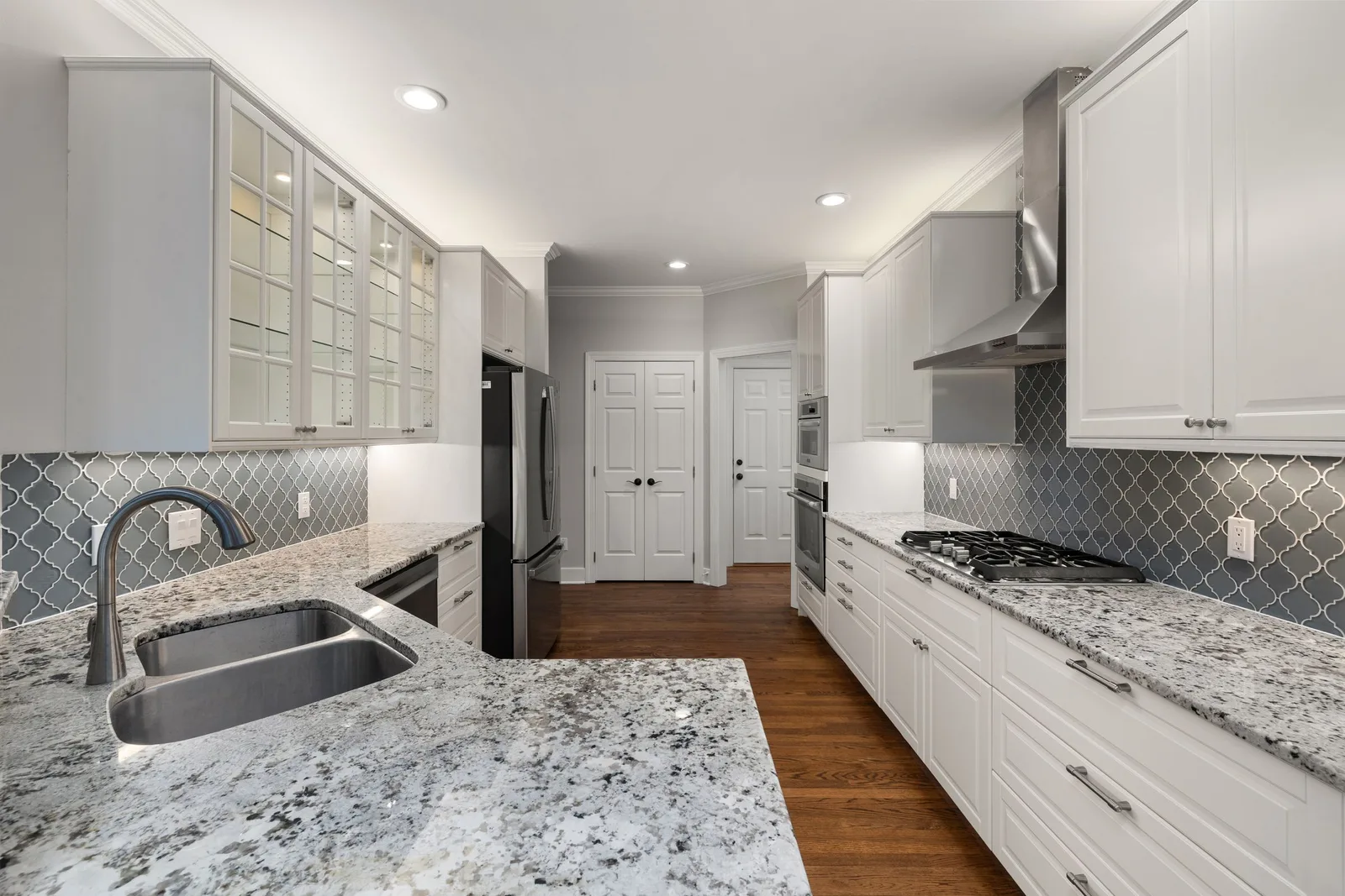 A white kitchen with granite counters, a gray tile backsplash and a gas cooktop