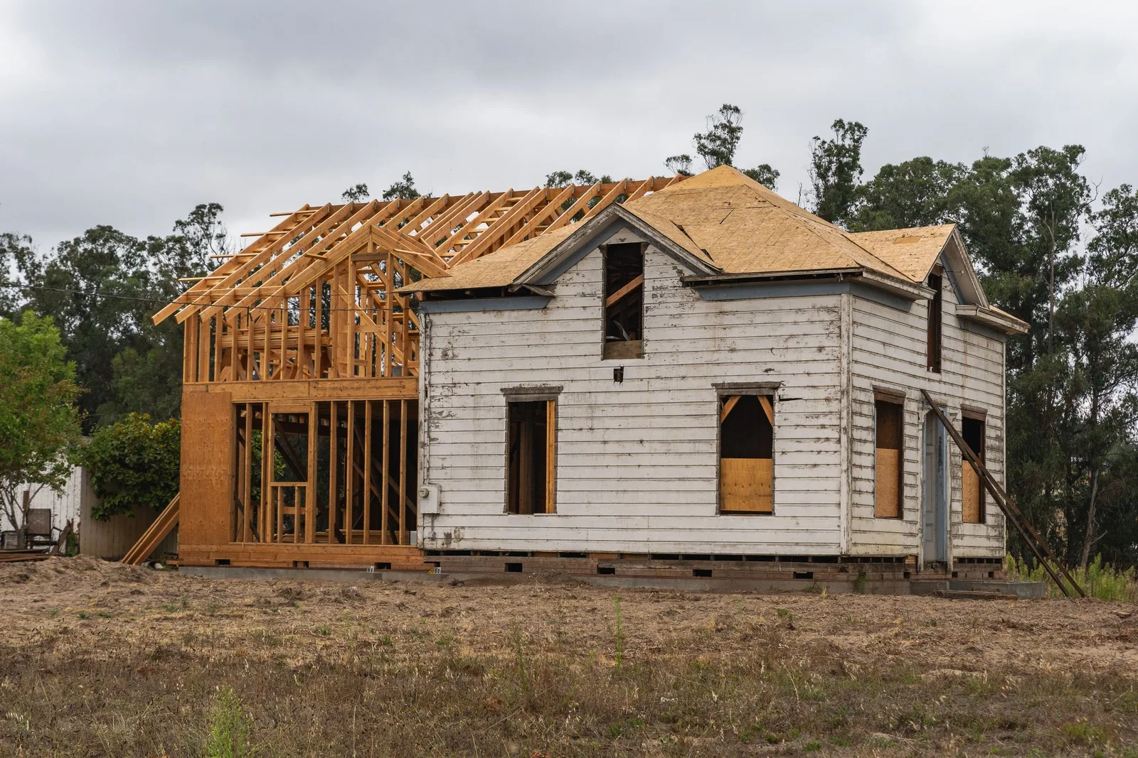An old white farmhouse with a new wood-framed addition and fresh roof sheathing