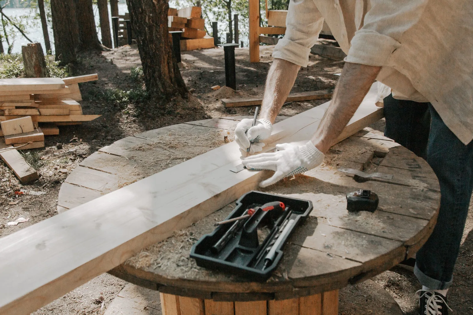 Gloved hands marking a board on a cable-spool table with a tool tray