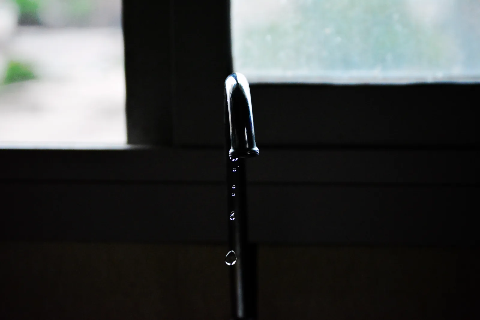 Water dripping from a tap in front of a window